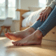 Personne assise sur le lit touche ses pieds dans une chambre lumineuse